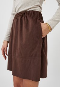 Gonna marrone in suede con fascia elastica in vita, tasca laterale e leggero taglio a A. Tessuto liscio e design alla lunghezza del ginocchio.