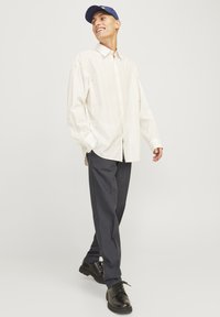 Langærmet, let stribet skjorte med knapper, som er parret med mørkegrå stribede bukser og sorte snøresko. En blå cap fuldender outfittet.