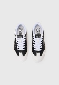Sorte og hvite joggesko laget av teksturert materiale, med hvit såle, hvite lisser og merkevare på siden. Minimalistisk design.