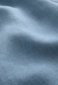 Tissu bleu clair avec une texture lisse et un subtil motif tissé ; présenté en doux plis, mettant en valeur sa chute et son éclat.