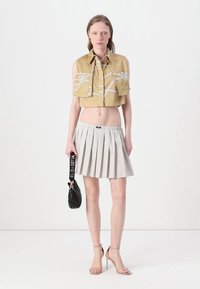 Camicia d'oro tagliata con motivi bianchi, gonna plissettata a pois e borsa nera. La modella indossa tacchi nudi. Design semplice e moderno.