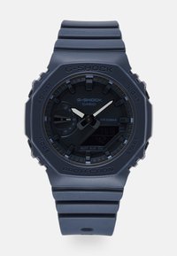 Analog-digital G-SHOCK klokke med et matt marineblått plasthus og rem. Har en svart skive med sølvdetaljer og flere funksjonsknapper.