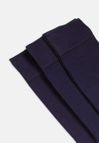Calcetines de color azul marino con textura suave, que presentan un puño reforzado y una puntera sin costuras. Tres pares apilados de manera ordenada.