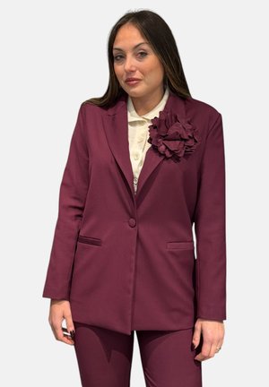 Abito bordeaux caratterizzato da un blazer aderente con un pulsante, tasche a busta e un accento floreale testurizzato sulla rever. Abbinato a pantaloni coordinati.