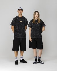 T-shirt con motivo in marmo nero e logo "JACKER", abbinata a pantaloni corti neri. Gli accessori includono sneakers nere e calze con logo, oltre a un cappellino bianco.
