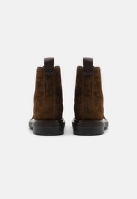 Brown suede ankle boots with a smooth black sole, featuring a pull tab and subtle branding on the side. Clean design with no embellishments.