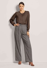 Bruine satijnen blouse met puffed sleeves en een ronde halslijn, gecombineerd met hooggereguleerde, grijs gestreepte broek en bruine hakken.