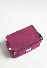 Lila kanvas necessär med dragkedja, gräddfärgade repdetaljer, rektangulär form och en vit etikett med varumärket.