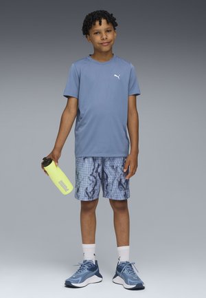 T-shirt de sport bleu, shorts bleu à motifs et baskets bleues. Tient une bouteille d'eau jaune. Design simple, matériaux légers.