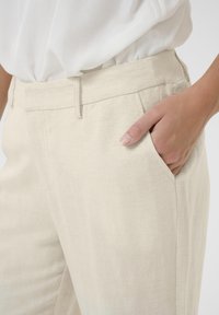 Pantalons en lin beige à coupe ajustée, avec des poches latérales et un devant plat. Comprend des coutures discrètes le long de la taille.