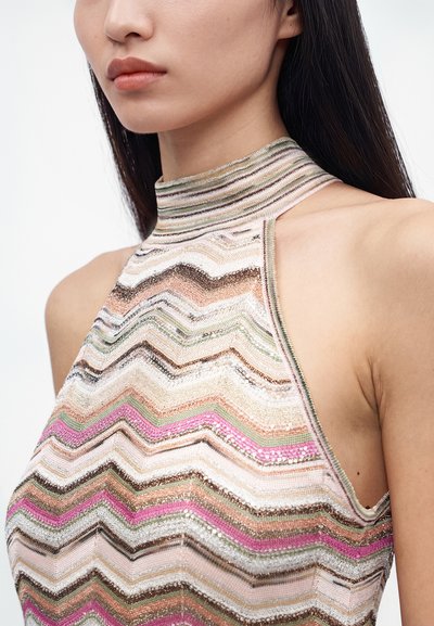 Femme portant un haut sans manches à col haut avec des motifs zigzag multicolores dans des tons rose, vert, marron et blanc.