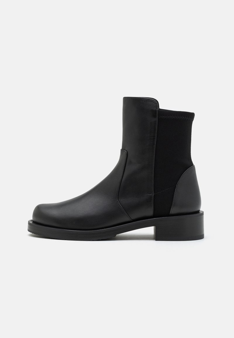 Bottine en cuir noir avec un bout arrondi, des panneaux latéraux élastiques et un talon épais. Texture lisse avec un design minimaliste.