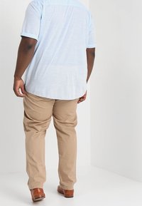 Jasnoniebieska koszula z krótkim rękawem o fakturowanej powierzchni, zestawiona z beżowymi spodniami i brązowymi butami, widziana od tyłu.