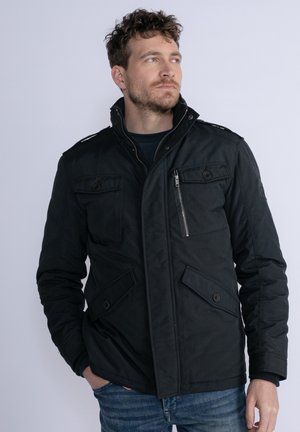 Schwarze isolierte Jacke mit hohem Kragen, mehreren Taschen, Reißverschluss und Knopfdetails. Der Stoff wirkt texturiert und strapazierfähig.