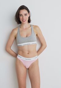 Soutien-gorge de sport en coton gris avec une bande logo Calvin Klein blanche, assorti à un string en coton rose pâle présentant une ceinture logo assortie.