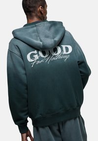 Felpa verde con cappuccio regolabile, caratterizzata dalla scritta "GOOD For Nothing" in bianco sul retro. Tessuto morbido, vestibilità rilassata.