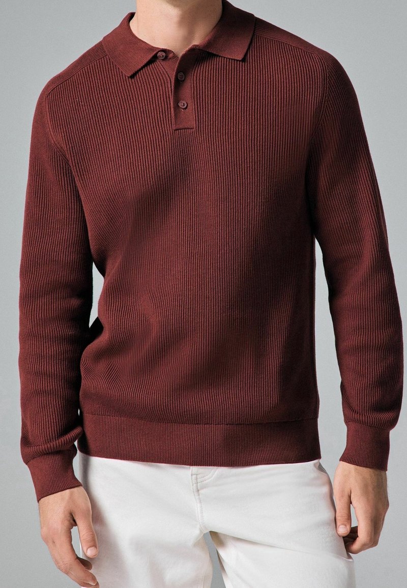 Pull en maille de couleur bordeaux avec un col polo, texture côtelée, manches longues et ourlet droit. Présente trois boutons au niveau du cou.