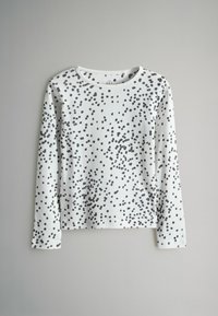 Ilga rankovė marškinėliai iš baltos medvilnės su juoda taškų raštu. Apvalus iškirpimas ir apatinė dalis, laisvas kirpimas, be matomų detalių ar akcentų.