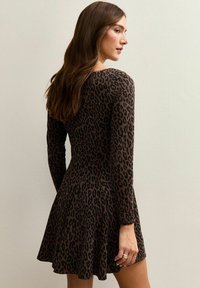 Vestido marrón con estampado de leopardo, de mangas largas, falda acampanada y textura acanalada. Tiene un escote redondo y un ajuste ceñido en el torso.