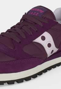 Μωβ αθλητικό παπούτσι Saucony Jazz με ταιριαστά κορδόνια, λευκό λογότυπο στο πλάι και ροζ όνομα μάρκας στη γλώσσα, κοντινή λήψη.