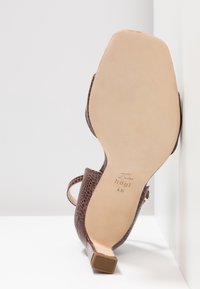 Sandale à talon haut marron à texture crocodile avec semelle beige, embout de talon carré et bride à la cheville, vue de dessous.