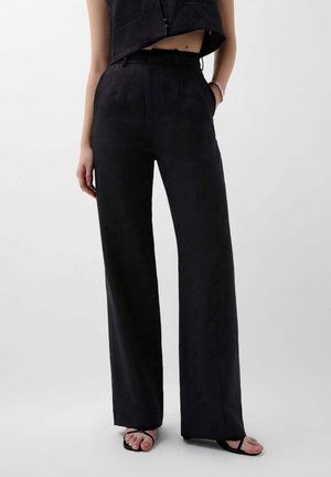 Pantaloni neri a gamba larga su misura in tessuto texture con vita alta, tasche laterali e una silhouette elegante. Abbinati a un top coordinato e sandali.