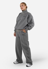 Gray fleece sweatshirt with half-zip and side pockets, paired with matching gray sweatpants. Both feature subtle branding accents.