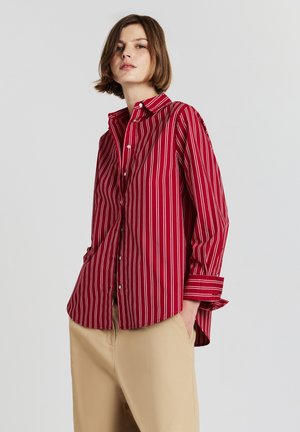 Red and white striped button-up shirt with a collar and long sleeves, paired with beige trousers. Features a relaxed fit and soft fabric.