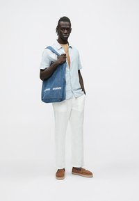 Spijkerstoffen totebag met witte tekst "SAMSØE", licht geruit kort shirt met korte mouwen, lichtbruine slip-ons en witte linnen broek.