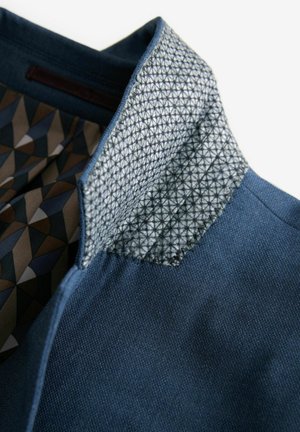 Collo di giacca di jeans blu con foderatura a motivo geometrico in tonalità di marrone, blu e grigio, caratterizzato da un design triangolare testurizzato.