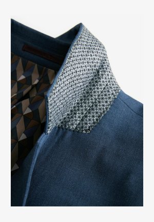 Culoarea gulerului jachetei din denim albastru este căptușită cu un model geometric în nuanțe de maroniu, albastru și gri, având un design texturat, în formă de triunghiuri.