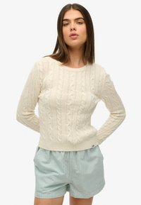 Crème kabelgebreide trui met lange mouwen en ronde halslijn, met een geribbelde zoom. Gepaard met blauw-witte gestreepte shorts.