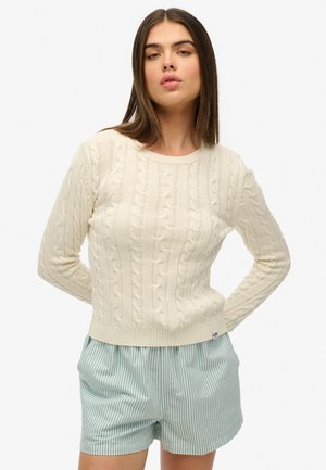 Crème kabelgebreide trui met lange mouwen en ronde halslijn, met een geribbelde zoom. Gepaard met blauw-witte gestreepte shorts.