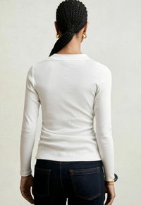 Tricou alb cu mânecă lungă din material ribbed, design mulat. Asortat cu blugi negri din denim, având buzunare la spate și cusături portocalii.