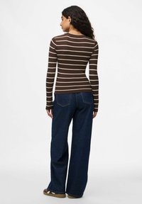 Maglia a maniche lunghe marrone a coste con strisce orizzontali crema, abbinata a jeans a gamba larga blu scuro e sneakers marroni. Vista posteriore mostrata.