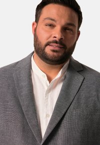 Szary żakiet z teksturowanej tkaniny, nałożony na białą koszulę z guzikami. Zdjęcie zbliżeniowe z neutralnym tłem.