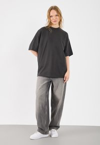 T-shirt preta de manga curta com um corte descontraído, combinada com jeans cinza claro de perna larga e ténis brancos sobre um fundo plain.