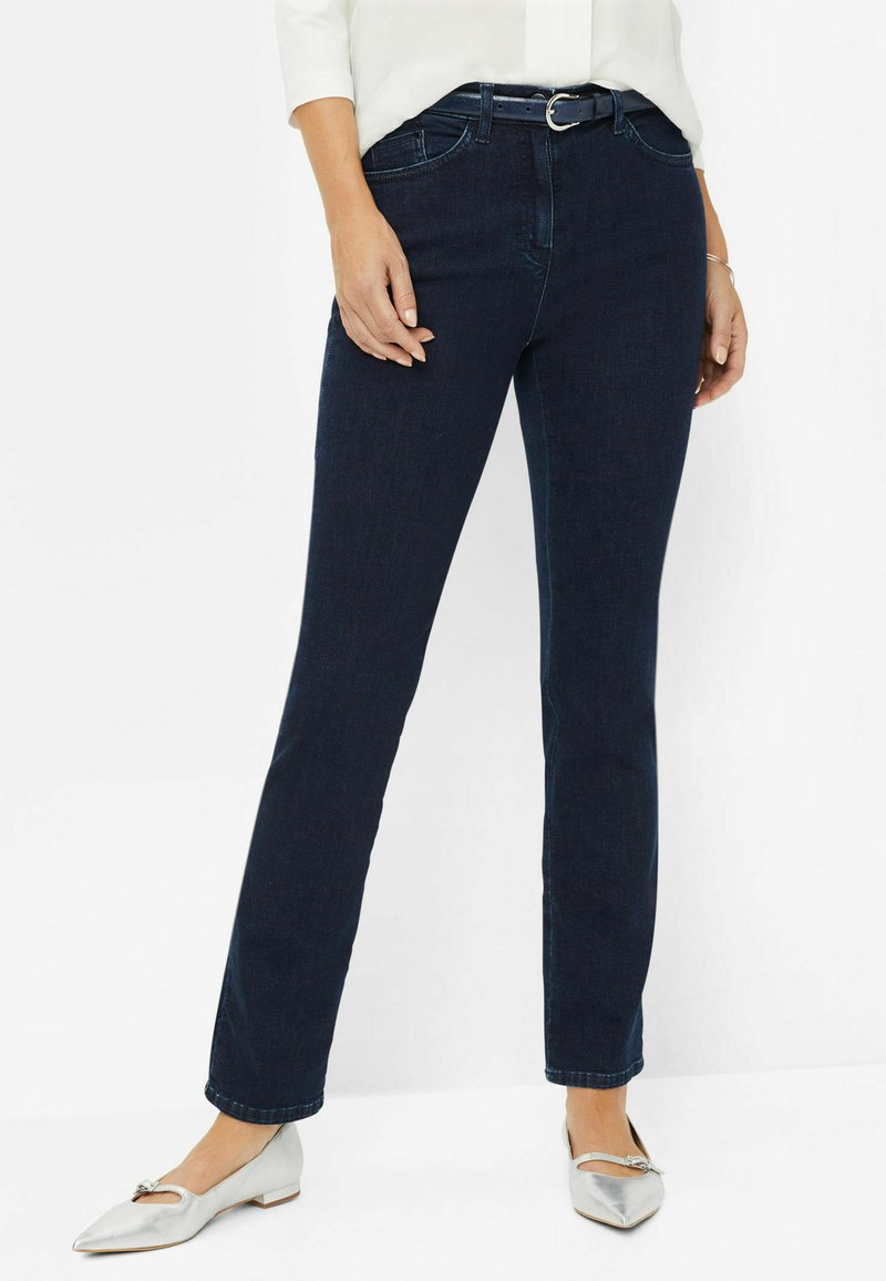Jean droit en denim foncé avec taille mi-haute, design à cinq poches et une ceinture avec boucle argentée. Associé avec des ballerines argentées.