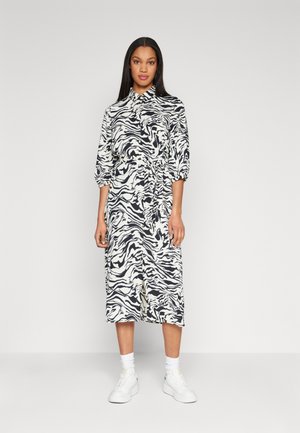 Robe midi à imprime zèbre noir et blanc, avec col et manches trois-quarts, taille cintrée, portée avec des baskets blanches. Texture de tissu lisse.