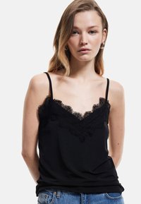 Schwarzes Top mit Spitzenbesatz am Kragen und dünnen Trägern. Weicher Stoff, taillierte Form und ein einfaches Design, kombiniert mit Jeans.