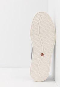 Semelle de chaussure avec un dessous en caoutchouc blanc texturé, présentant un motif ondulé et des contours arrondis. Partie sup érieure noire partiellement visible.