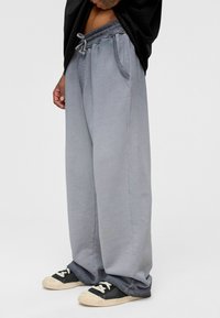 Lichtgrijze wijde broek met elastische koordsluiting in de taille, zijzakken en een gestructureerde afwerking, gecombineerd met zwarte sneakers.