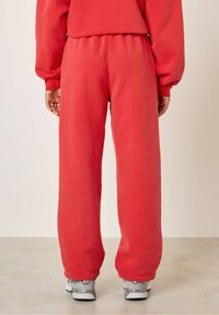 Punased dressipüksid, millel on mugav lõike, elastne vöökoht ja mansetiga äärised. Kangas näeb välja pehme; kantud hallide tennisetossudega.