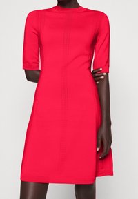 Robe rouge à manches courtes, avec des rayures verticales texturées et une silhouette cintrée. Confectionnée en tissu extensible, longueur aux genoux.