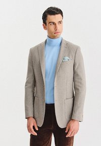 Szary żakiet w kominowy wzór, noszony na jasnoniebieskim golfie, zestawiony z brązowymi spodniami sztruksowymi, z niebiesko-białą poszetką.