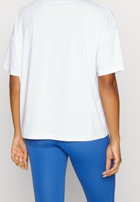 Camiseta blanca de manga corta con un corte relajado, hecha de una tela suave, combinada con leggings azules que tienen un ligero brillo.