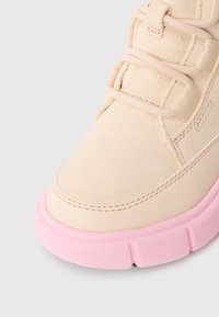 Beige treningstøvel med teksturert overdel, snøring og rosa gummisåle. Har avrundet tå og synlig søm for ekstra detalj.