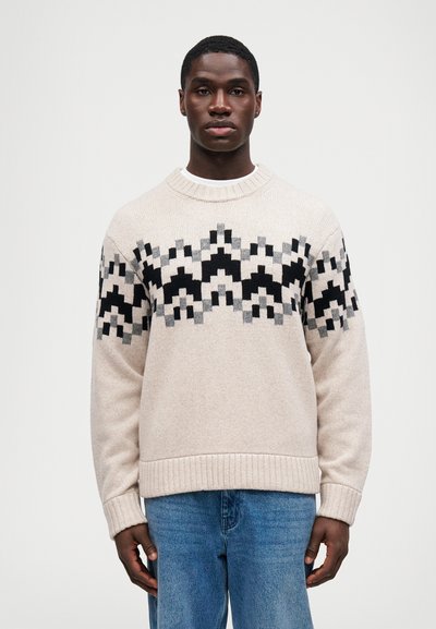 Beige strikket trøje med rund hals og ribbede mansjetter, der har et geometrisk sort og gråt mønster på brystet og ærmerne.
