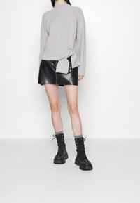 Ljusgrå ribbstickad tröja med sidoband, kombinerad med en svart minikjol i läder med en dragkedja framtill och svarta snörstövlar med grå mudd.