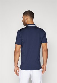 Polo à manches courtes marine avec un col blanc; tissu lisse; design ajusté mettant en valeur les contours des épaules et du dos.
